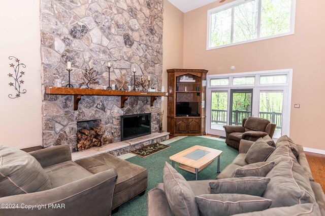 living room featuring a stone fireplace, baseboards, a towering ceiling, and wood finished floors