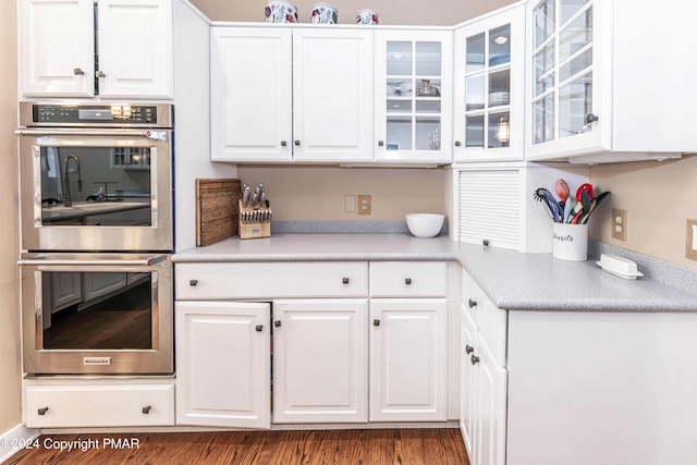 kitchen with wood finished floors, light countertops, glass insert cabinets, white cabinetry, and double oven