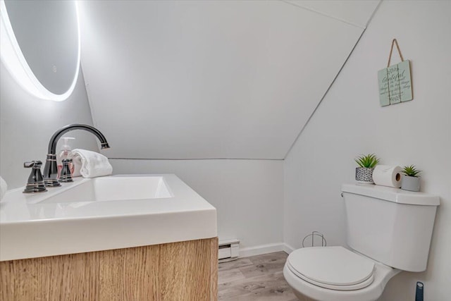 bathroom featuring toilet, a sink, wood finished floors, baseboard heating, and vaulted ceiling