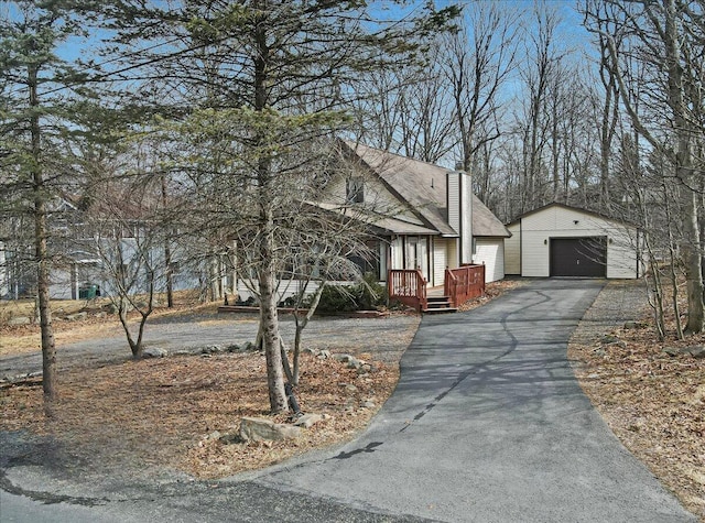 view of front of house with an outbuilding, a garage, a chimney, and aphalt driveway