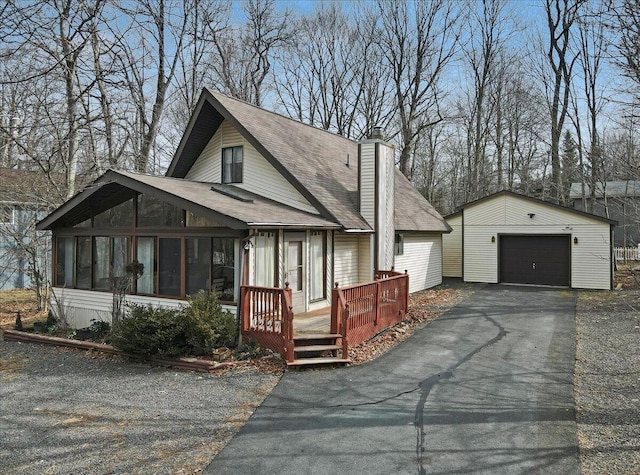 view of front of house featuring an outbuilding, driveway, a shingled roof, a garage, and a chimney