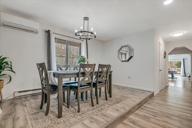 dining space with a notable chandelier, light wood-style floors, a wall unit AC, and a baseboard radiator