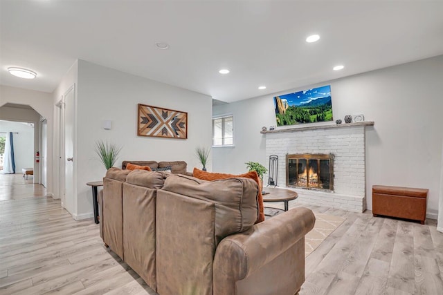 living area with arched walkways, recessed lighting, light wood finished floors, and a brick fireplace