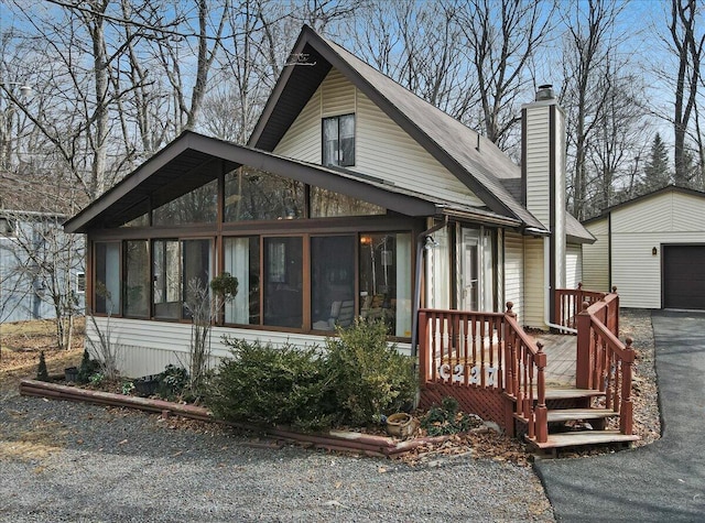 view of front of property featuring aphalt driveway, an outbuilding, a garage, and a sunroom