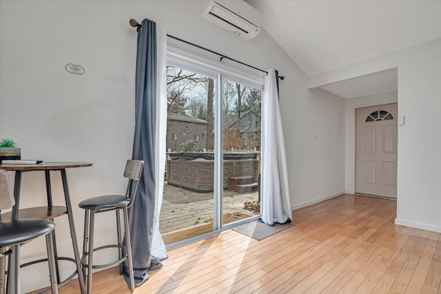 unfurnished dining area featuring a wall unit AC, baseboards, light wood-type flooring, and lofted ceiling