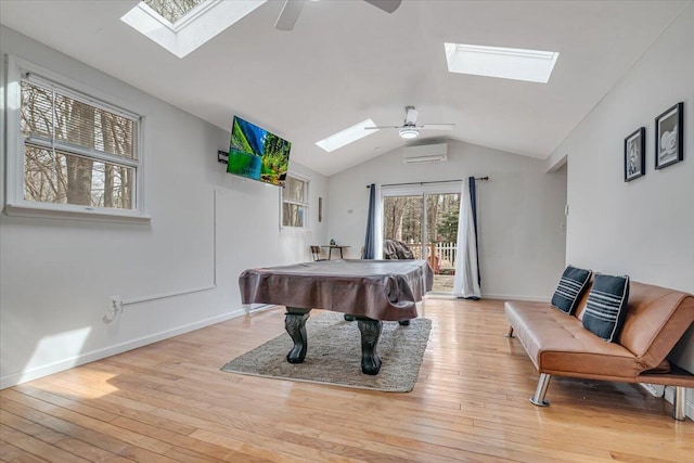 game room featuring a wall mounted AC, lofted ceiling with skylight, light wood-type flooring, and ceiling fan