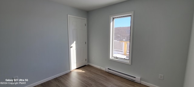 spare room featuring a baseboard radiator, baseboards, and wood finished floors