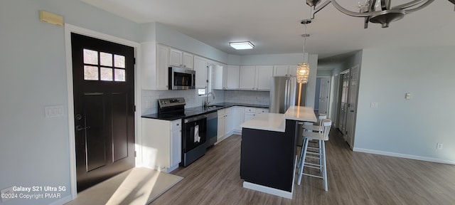 kitchen featuring backsplash, appliances with stainless steel finishes, white cabinetry, a sink, and a kitchen breakfast bar