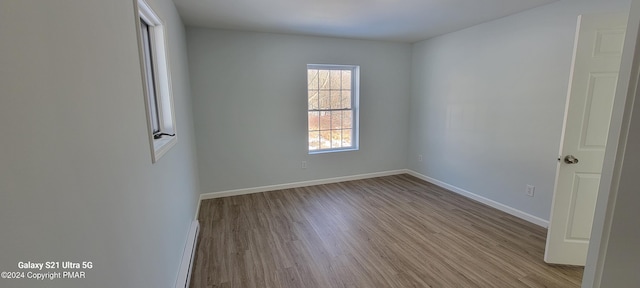 empty room with a baseboard radiator, wood finished floors, and baseboards