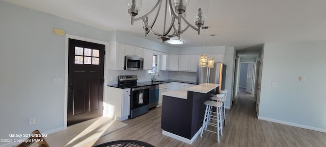 kitchen featuring appliances with stainless steel finishes, backsplash, an inviting chandelier, white cabinetry, and a sink