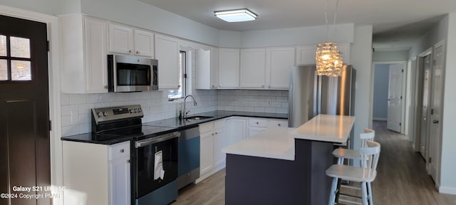 kitchen with a kitchen island, a sink, a kitchen breakfast bar, appliances with stainless steel finishes, and light wood finished floors