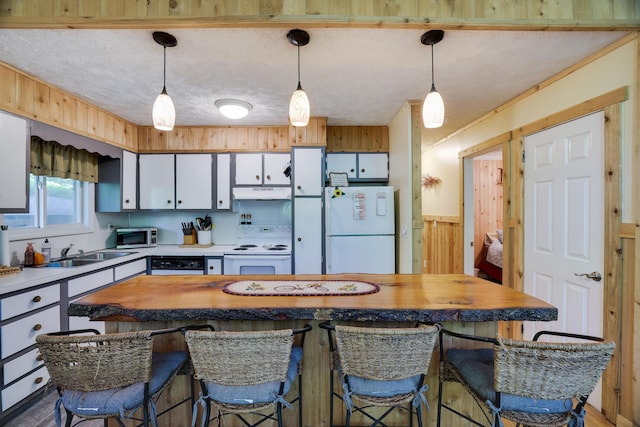 354 Fawn Rd, Pocono Lake, PA 18347 - kitchen featuring white appliances, under cabinet range hood, white cabinets, wood walls, and decorative light fixtures
