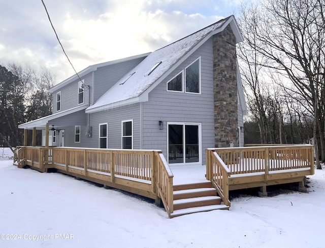 snow covered back of property featuring a shingled roof, a chimney, and a wooden deck