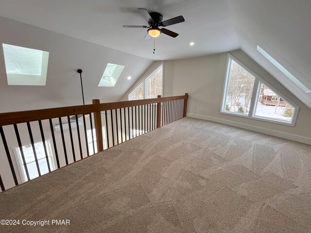 additional living space featuring carpet, vaulted ceiling with skylight, baseboards, and ceiling fan