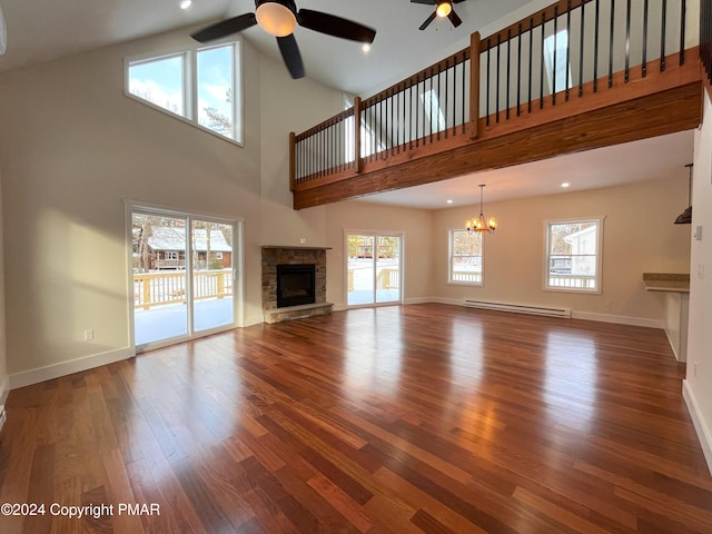 unfurnished living room featuring a healthy amount of sunlight, a baseboard heating unit, wood finished floors, and a stone fireplace