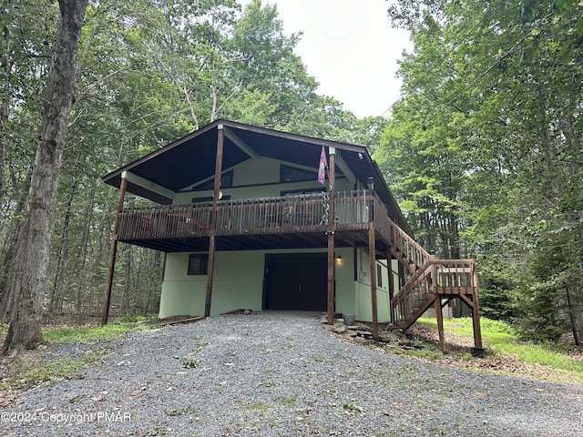 view of front of house with stairway, a wooded view, driveway, a wooden deck, and an attached garage