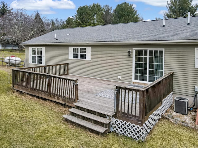 rear view of house with cooling unit, roof with shingles, a wooden deck, and a lawn