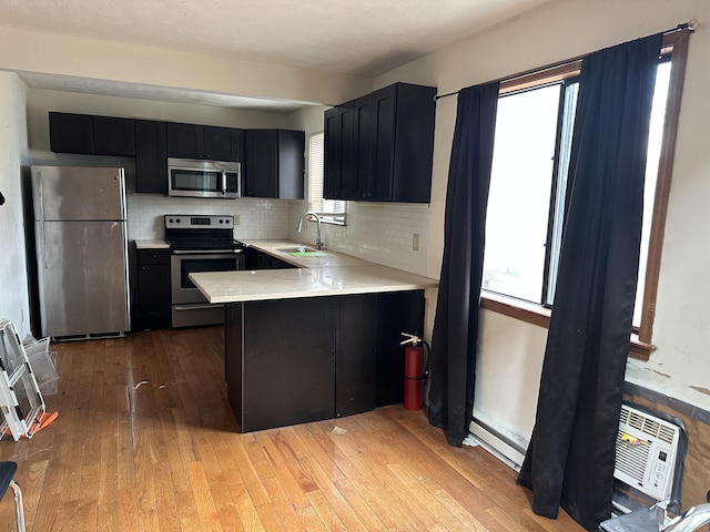 kitchen with light wood-type flooring, a sink, dark cabinetry, appliances with stainless steel finishes, and light countertops