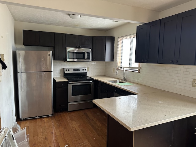 kitchen featuring a sink, a peninsula, a textured ceiling, stainless steel appliances, and dark wood-style flooring