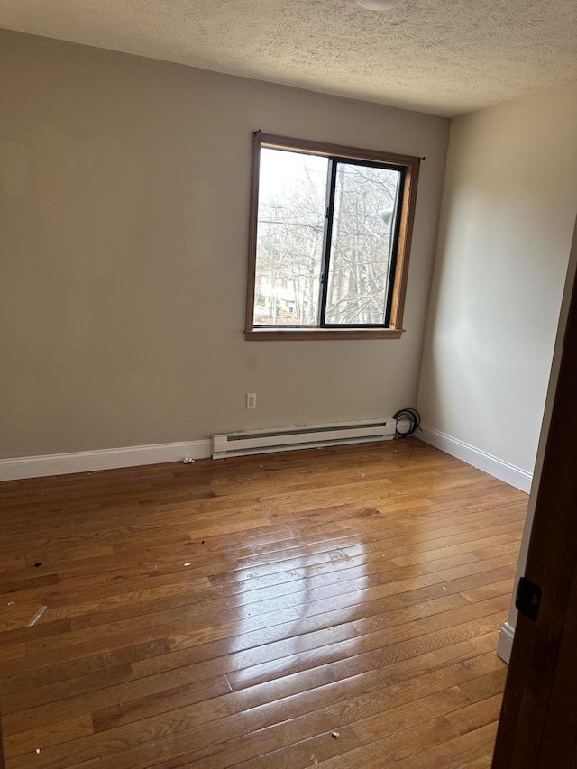 unfurnished room with baseboard heating, a textured ceiling, baseboards, and wood-type flooring