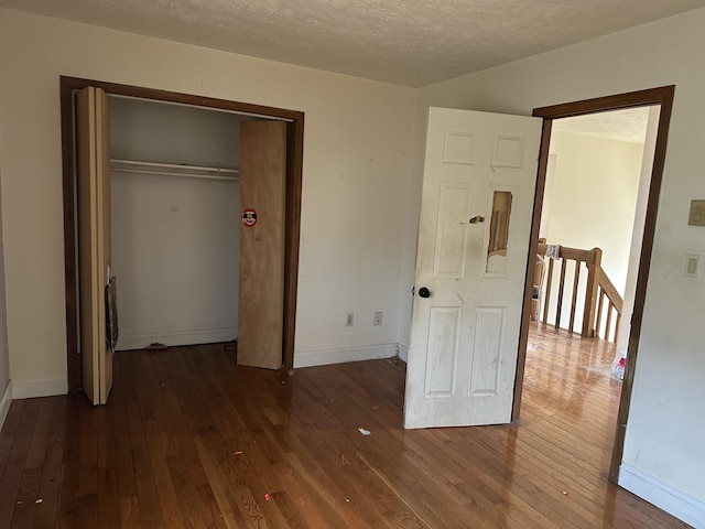 unfurnished bedroom with dark wood-style floors, a closet, a textured ceiling, and baseboards