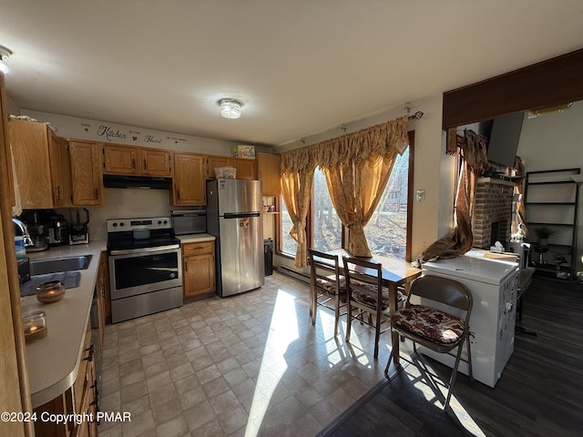 kitchen with a fireplace, a sink, stainless steel appliances, light countertops, and under cabinet range hood