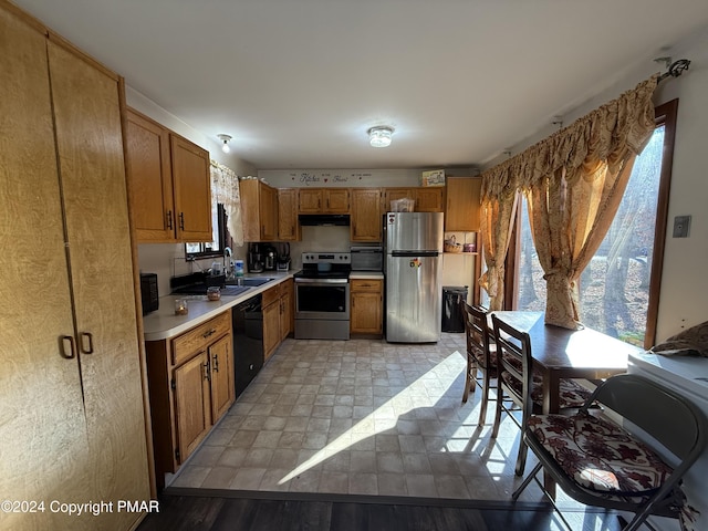 kitchen with brown cabinets, under cabinet range hood, a sink, stainless steel appliances, and light countertops