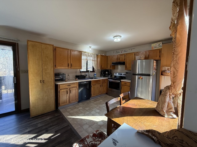 kitchen with under cabinet range hood, light floors, light countertops, stainless steel appliances, and a sink