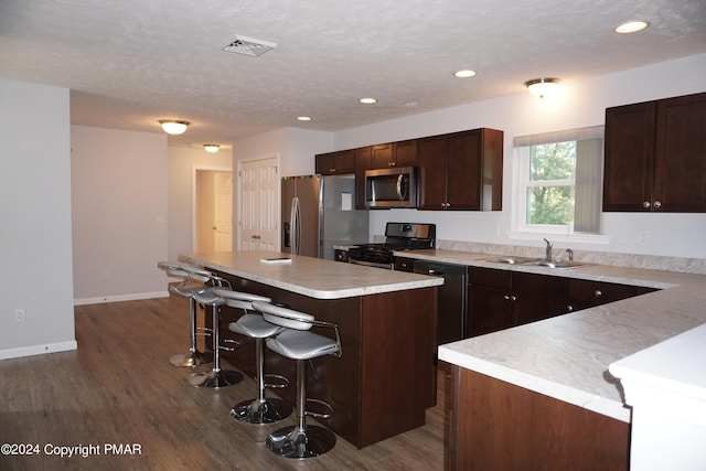 kitchen featuring dark brown cabinetry, a breakfast bar, sink, a center island, and appliances with stainless steel finishes