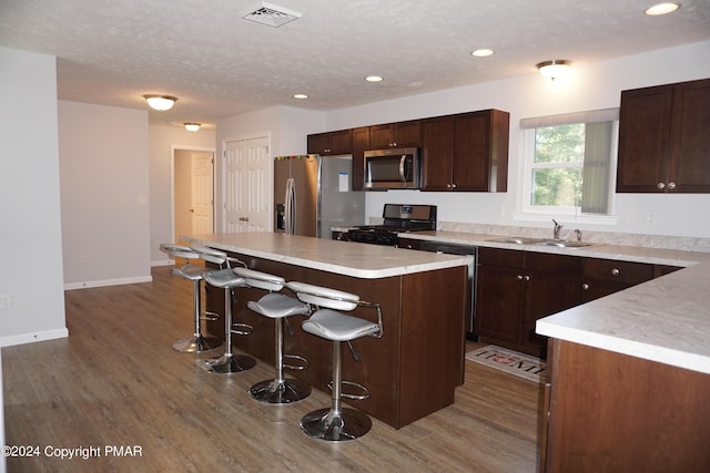 kitchen with a kitchen island, sink, a breakfast bar area, stainless steel appliances, and a textured ceiling