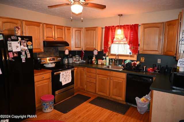 kitchen with light wood finished floors, dark countertops, under cabinet range hood, black appliances, and a sink