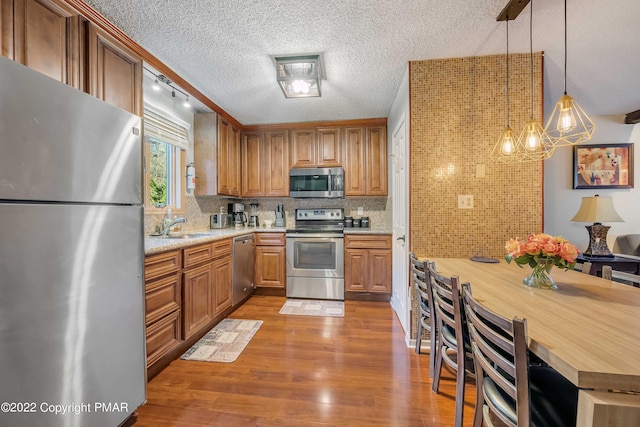 kitchen featuring tasteful backsplash, hanging light fixtures, stainless steel appliances, light stone countertops, and light wood-type flooring