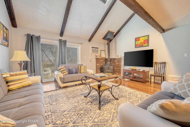 living room featuring vaulted ceiling with beams, a textured ceiling, an AC wall unit, a wood stove, and hardwood / wood-style flooring