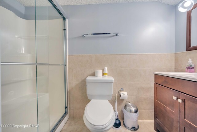 bathroom with tile walls, vanity, a textured ceiling, a shower with shower door, and toilet