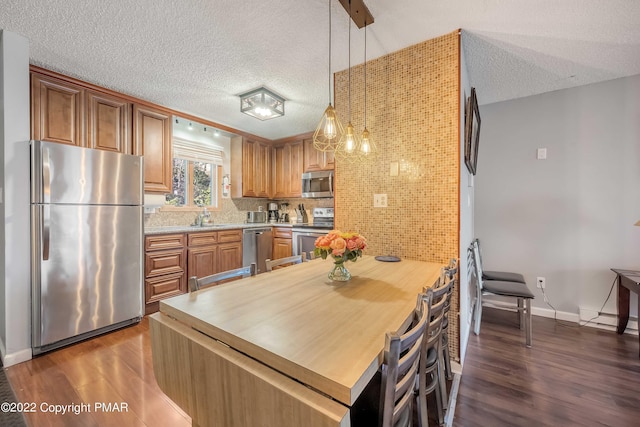 kitchen with dark hardwood / wood-style floors, pendant lighting, sink, decorative backsplash, and stainless steel appliances