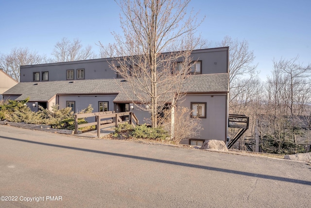 townhome / multi-family property featuring a shingled roof, fence, and stucco siding