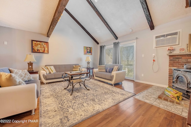 living room with lofted ceiling with beams, a wood stove, a wall unit AC, hardwood / wood-style flooring, and a textured ceiling