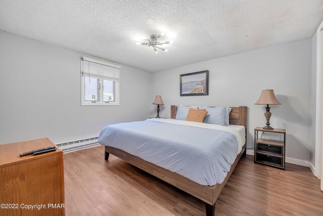 bedroom with wood-type flooring, a baseboard heating unit, and a textured ceiling