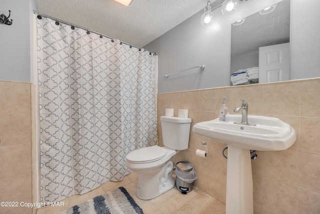 bathroom with toilet, a textured ceiling, tile walls, a shower with shower curtain, and tile patterned flooring