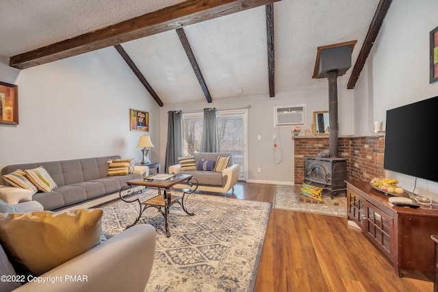 living area with lofted ceiling with beams, wood finished floors, a wood stove, a textured ceiling, and an AC wall unit