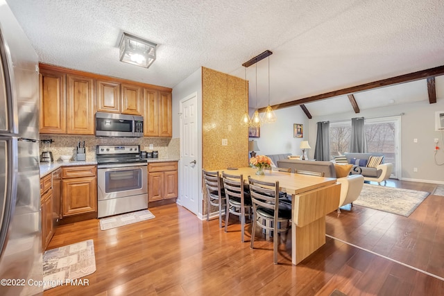 kitchen with tasteful backsplash, appliances with stainless steel finishes, hardwood / wood-style floors, and hanging light fixtures