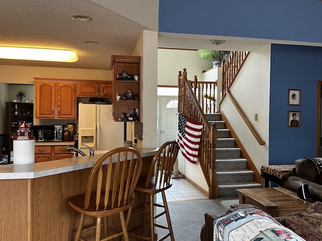 kitchen featuring a kitchen breakfast bar, white refrigerator with ice dispenser, a sink, black microwave, and brown cabinets