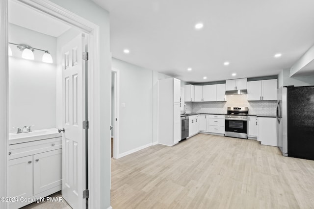 kitchen featuring light wood-style flooring, under cabinet range hood, stainless steel appliances, a sink, and backsplash