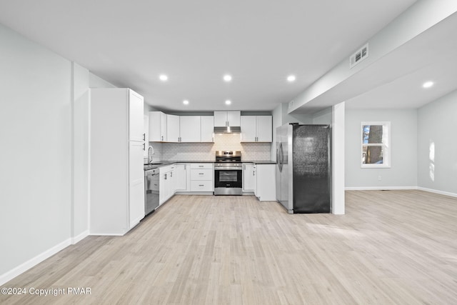 kitchen with appliances with stainless steel finishes, a sink, light wood-style floors, and decorative backsplash