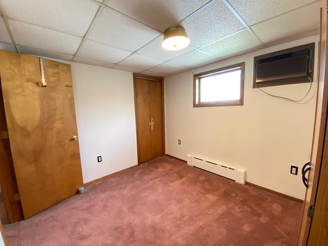 below grade area featuring carpet, a wall unit AC, a baseboard heating unit, and a drop ceiling