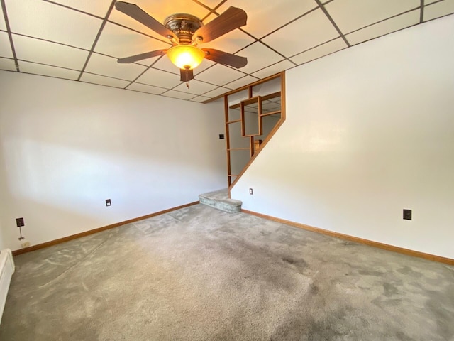carpeted empty room with ceiling fan, a drop ceiling, and baseboards