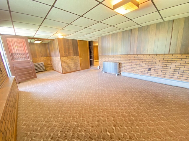 interior space with carpet floors, a paneled ceiling, radiator heating unit, and brick wall