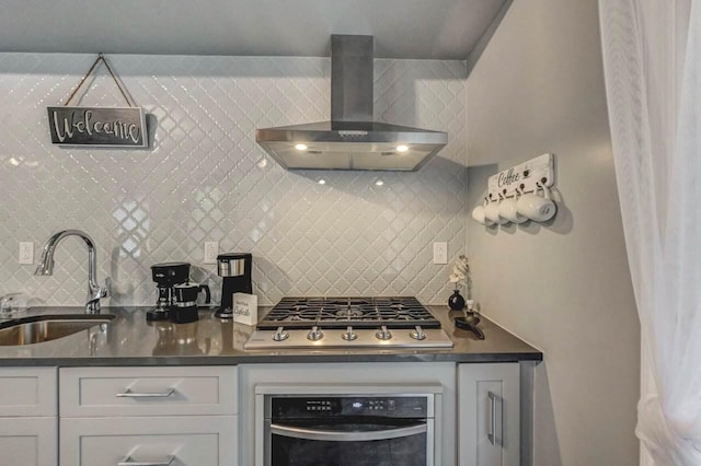 kitchen with a sink, wall oven, wall chimney exhaust hood, stainless steel gas cooktop, and tasteful backsplash