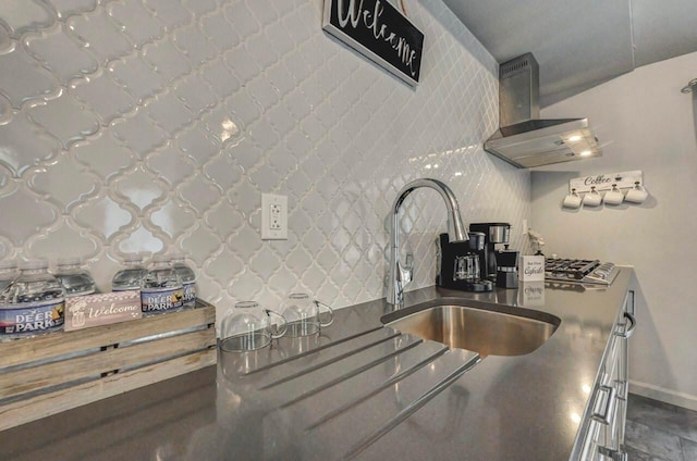 kitchen featuring a sink, wall chimney exhaust hood, baseboards, and dark countertops