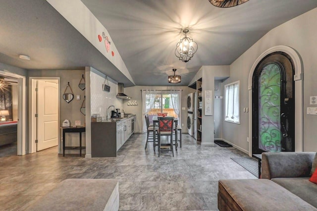 dining space with estacked washer and dryer, baseboards, a chandelier, arched walkways, and lofted ceiling